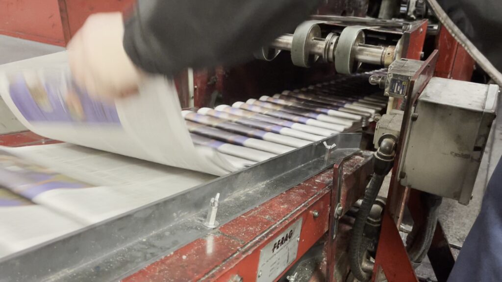 A press operator swoops in to get grab a fast-moving newspaper in order to inspect it for color and registration at the Cleveland Plain Dealer printing facility on November 19, 2024. Photo by Richard Alan Hannon